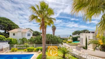 Vue extérieure depuis la Villa Estrella montrant une piscine au premier plan, des palmiers, des balustrades blanches et des villas voisines sous un ciel bleu parsemé de quelques nuages.