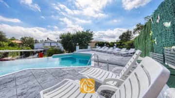 Piscine privée avec de nombreux bains de soleil en plastique blanc sur une terrasse carrelée à la Villa Geolouk en Espagne.