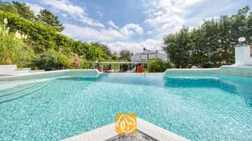 Piscine carrelée privée à la Villa Geolouk, entourée d'arbres verdoyants, d'arbustes et d'un ciel bleu parsemé de nuages.