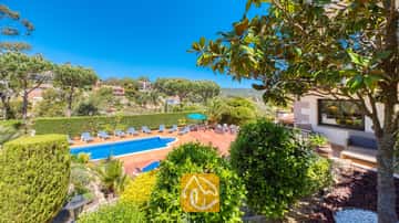 Terrasse extérieure de la Villa Jaruco dotée d'une piscine bleue bordée de transats à rayures et entourée d'arbres verdoyants sous un ciel d'un bleu éclatant