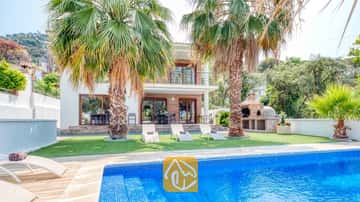 Piscine privée ornée de carreaux de mosaïque bleue et transats sur la pelouse à la Villa Marcella, agrémentée de palmiers et d'un barbecue en brique.