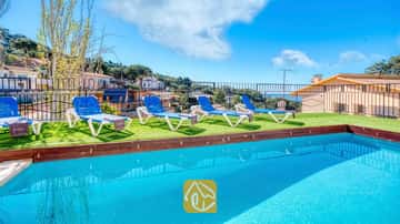 Piscine extérieure à l'eau bleu vif à la Villa Donna, dotée de quatre transats blancs et bleus sur gazon synthétique sous un ciel dégagé.