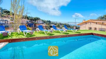 Piscine extérieure à l'eau bleu vif à la Villa Donna, dotée de quatre transats blancs et bleus sur gazon synthétique sous un ciel dégagé.