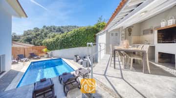 Extérieur de la Villa Rosa comprenant une piscine bleue, des chaises longues et une terrasse-salle à manger couverte en plein air avec un barbecue intégré.