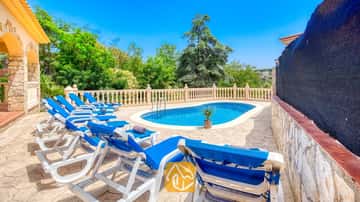 Piscine extérieure privée à la Villa Sarai, entourée de bains de soleil bleus, d'un patio en pierre et d'arbres verdoyants sous un ciel d'un bleu éclatant