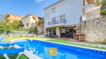 Piscine privée avec transats bleus et terrasse en pierre à la Villa Nicky, dotée d'un extérieur blanc à étages, d'un barbecue extérieur et d'un espace repas sur une terrasse ouverte.