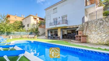 Piscine privée avec transats bleus et terrasse en pierre à la Villa Nicky, dotée d'un extérieur blanc à étages, d'un barbecue extérieur et d'un espace repas sur une terrasse ouverte.