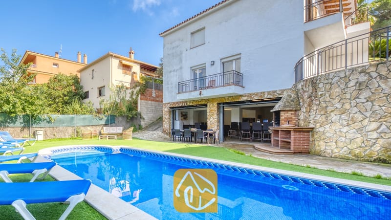 Piscine privée avec transats bleus et terrasse en pierre à la Villa Nicky, dotée d'un extérieur blanc à étages, d'un barbecue extérieur et d'un espace repas sur une terrasse ouverte.