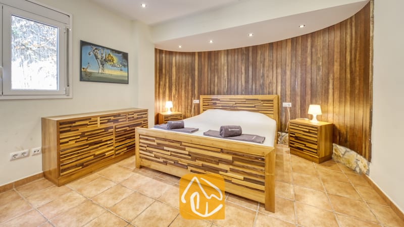 Chambre à coucher dotée d'un lit avec un cadre en bois, de tables de chevet assorties surmontées de lampes, et d'un mur d'accent incurvé en lattes de bois derrière le lit.