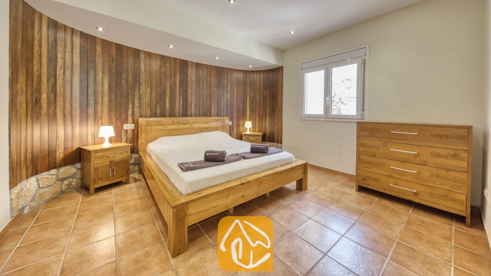 Chambre à coucher dotée d'un lit double en bois, de tables de chevet assorties avec lampes, et d'un mur d'accent en lambris de bois vertical derrière la tête de lit.