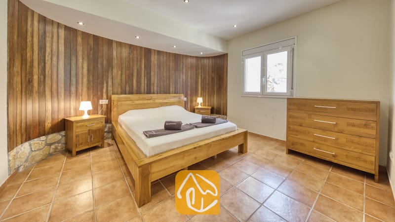 Chambre à coucher dotée d'un lit double en bois, de tables de chevet assorties avec lampes, et d'un mur d'accent en lambris de bois vertical derrière la tête de lit.