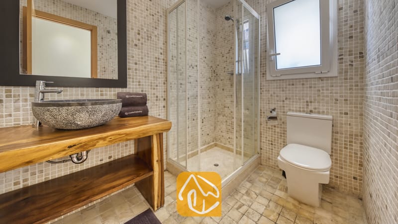 Salle de bain moderne dotée d'une douche d'angle vitrée, d'une vasque en pierre posée sur un meuble sous-lavabo en bois brut aux bords naturels, et de murs en mosaïque beige.