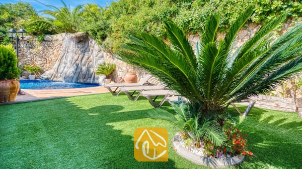 Jardin luxuriant et verdoyant de la Villa Alba, doté de gazon synthétique, d'un palmier cycas remarquable, de chaises longues et d'un plan d'eau en pierre agrémenté d'une cascade.