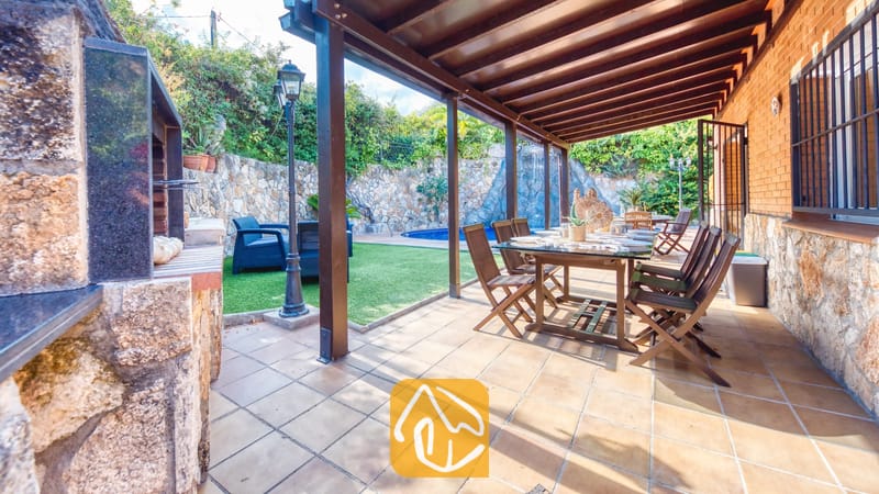 Terrasse repas extérieure couverte à la Villa Alba, dotée d'une table et de chaises de salle à manger en bois, d'un sol carrelé et d'un espace barbecue intégré attenant, offrant une vue sur le jardin et la piscine.