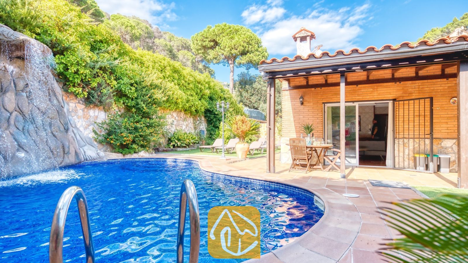 Piscine privée dotée d'une cascade en roches naturelles à la Villa Alba, mettant en valeur un patio extérieur en briques avec un mobilier de salle à manger en bois et un toit en tuiles.