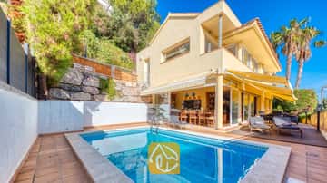 Piscine privée à la Villa Santa Cristina, agrémentée d'une terrasse carrelée, de stores jaunes et de chaises longues sur un deck en bois jouxtant la façade jaune de la propriété.
