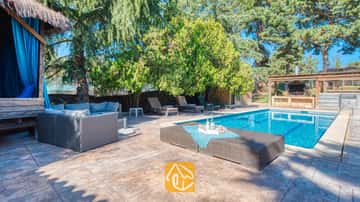 Piscine extérieure privée à la Villa Can Bernardi, dotée d'un canapé en résine tressée grise, de chaises longues et d'un espace barbecue extérieur entouré d'arbres.