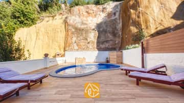 Piscine privée à la Villa Blanca ornée de carreaux de mosaïque bleus, située sur une terrasse pavée bordée d'une haute paroi rocheuse et agréposandée de chaises longues en bois dotées de coussins violets.