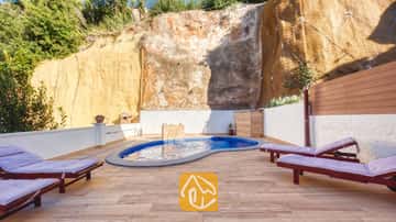 Piscine privée à la Villa Blanca ornée de carreaux de mosaïque bleus, située sur une terrasse pavée bordée d'une haute paroi rocheuse et agréposandée de chaises longues en bois dotées de coussins violets.