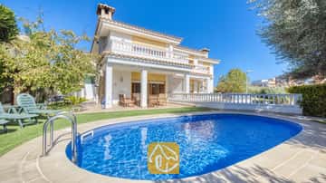 Piscine privée aux eaux bleues et aux mains courantes en métal devant l'extérieur de la Villa Baileys à deux étages, qui arbore des colonnes blanches, des balcons et un toit en tuiles sous un ciel dégagé.