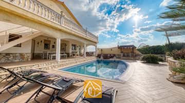 Piscine privée avec chaises longues sur la terrasse pavée de la Villa Madonna en Espagne, dotée d'un patio couvert et de murs en pierre sous un ciel ensoleillé