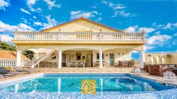 Vue extérieure de la Villa Madonna mettant en valeur une piscine dotée d'une mosaïque de dauphin, une véranda ombragée, un patio en pierre et des murs extérieurs jaunes sous un ciel bleu.