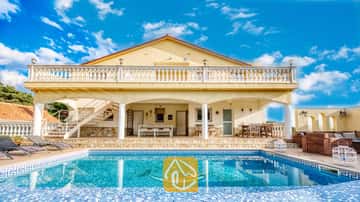Vue extérieure de la Villa Madonna mettant en valeur une piscine dotée d'une mosaïque de dauphin, une véranda ombragée, un patio en pierre et des murs extérieurs jaunes sous un ciel bleu.