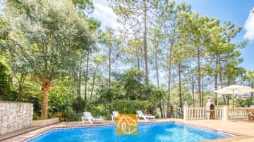 Piscine privée à la Villa Esmee avec des chaises longues blanches sur la terrasse carrelée, entourée de grands pins et dotée d'un barbecue en pierre.
