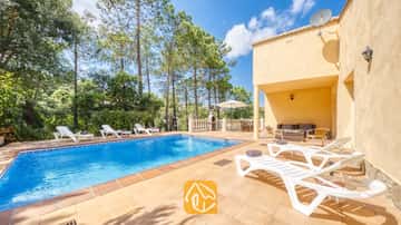 Piscine extérieure privée à la Villa Esmee, avec des chaises longues blanches sur une terrasse carrelée, entourée de pins sous un ciel bleu.