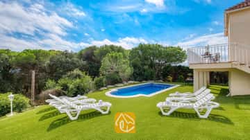 Piscine extérieure entourée d'une pelouse verdoyante et de transats blancs à la Villa La Luna, en Espagne, avec en toile de fond des arbres et un ciel bleu.