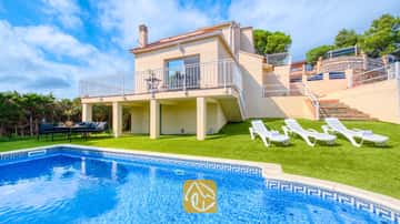 Extérieur de la Villa La Luna mettant en valeur une piscine privée, des transats blancs sur gazon synthétique et une maison beige à deux étages avec balcon sous un ciel partiellement nuageux.