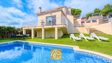 Extérieur de la Villa La Luna mettant en valeur une piscine privée, des transats blancs sur gazon synthétique et une maison beige à deux étages avec balcon sous un ciel partiellement nuageux.