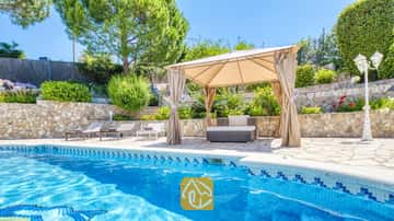 Piscine privée à la Villa Lorena avec margelles en carrelage bleu, tonnelle en tissu beige surplombant le salon de jardin, murs de soutènement en pierre et végétation environnante.