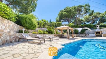 Piscine privée avec chaises longues et terrasse en pierre à la Villa Lorena, entourée de pins, de jardins en terrasses et d'un gazebo ombragé.