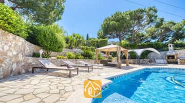 Piscine privée avec chaises longues et terrasse en pierre à la Villa Lorena, entourée de pins, de jardins en terrasses et d'un gazebo ombragé.