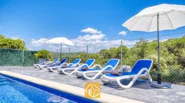Des transats blancs et bleus alignés au bord de la piscine de la Villa Fransisca, accompagnés de parasols blancs se détachant sur un ciel bleu.