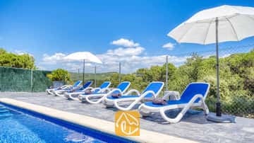 Des transats blancs et bleus alignés au bord de la piscine de la Villa Fransisca, accompagnés de parasols blancs se détachant sur un ciel bleu.