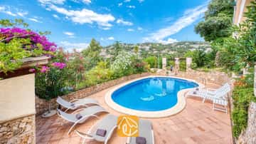 Piscine privée avec chaises longues et terrasse carrelée à la Villa Cleo en Espagne, entourée de murs en pierre et d'arbustes en fleurs.