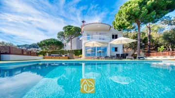 L'extérieur de la Villa Chanel dévoile une piscine turquoise, des parasols blancs sur la terrasse et un balcon en pierre aux lignes courbes, le tout niché au cœur d'une pinède luxuriante.