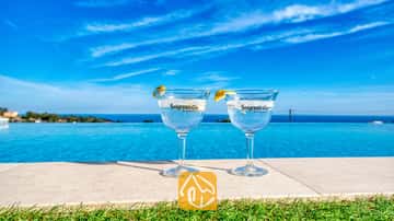 Deux cocktails au gin agrémentés de rondelles de citron au bord de la piscine à débordement de la Villa Chanel, avec vue sur la mer et le ciel azur.