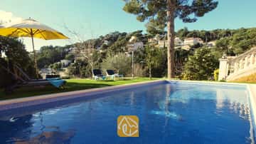 Piscine privée bordée de carrelage bleu à la Villa Noa, avec des chaises longues sur la pelouse et une vue imprenable sur les collines sous un ciel dégagé.