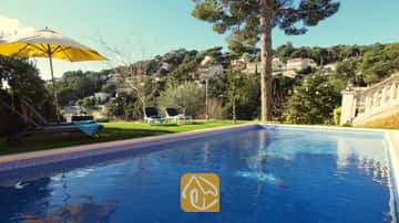 Piscine privée bordée de carrelage bleu à la Villa Noa, avec des chaises longues sur la pelouse et une vue imprenable sur les collines sous un ciel dégagé.