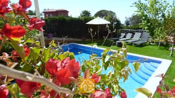 La piscine privée de la Villa Noa, encadrée de bougainvilliers rouges, avec des chaises longues et un parasol blanc sur la pelouse en arrière-plan.