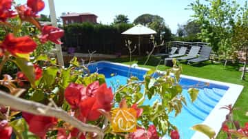 La piscine privée de la Villa Noa, encadrée de bougainvilliers rouges, avec des chaises longues et un parasol blanc sur la pelouse en arrière-plan.