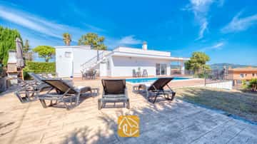 Piscine extérieure privée à la villa Yara, entourée de bains de soleil sombres sur une terrasse pavée sous un ciel bleu éclatant.