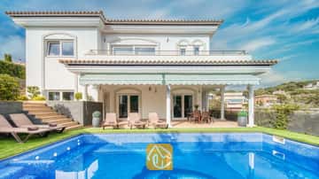Vue extérieure de la Villa Madison mettant en valeur une piscine carrelée de bleu, des chaises longues et une terrasse couverte aux colonnes blanches sur fond de ciel bleu azur.