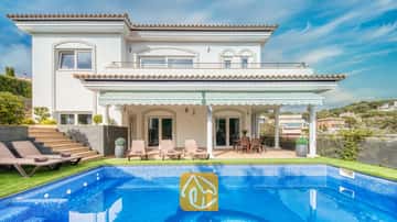 Vue extérieure de la Villa Madison mettant en valeur une piscine carrelée de bleu, des chaises longues et une terrasse couverte aux colonnes blanches sur fond de ciel bleu azur.