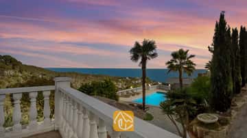 Terrasse surplombant la Villa Tropicana avec piscine privée, palmiers et vue sur la mer sous un ciel de couchant aux teintes roses et bleues.
