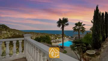 Terrasse surplombant la Villa Tropicana avec piscine privée, palmiers et vue sur la mer sous un ciel de couchant aux teintes roses et bleues.