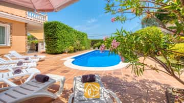 Piscine extérieure privée à la Villa Primavera, entourée d'une terrasse carrelée, de chaises longues blanches agrémentées de serviettes sombres enroulées et de branches de lauriers roses en fleurs.